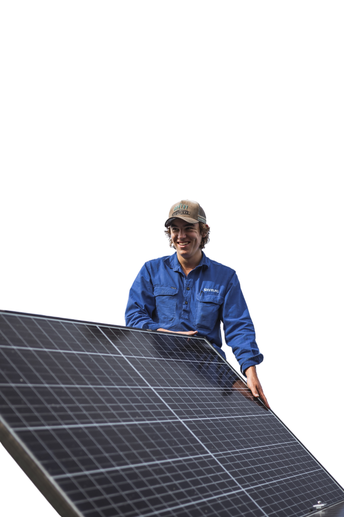 A person in a blue uniform and cap is holding and examining a large solar panel against a black background.