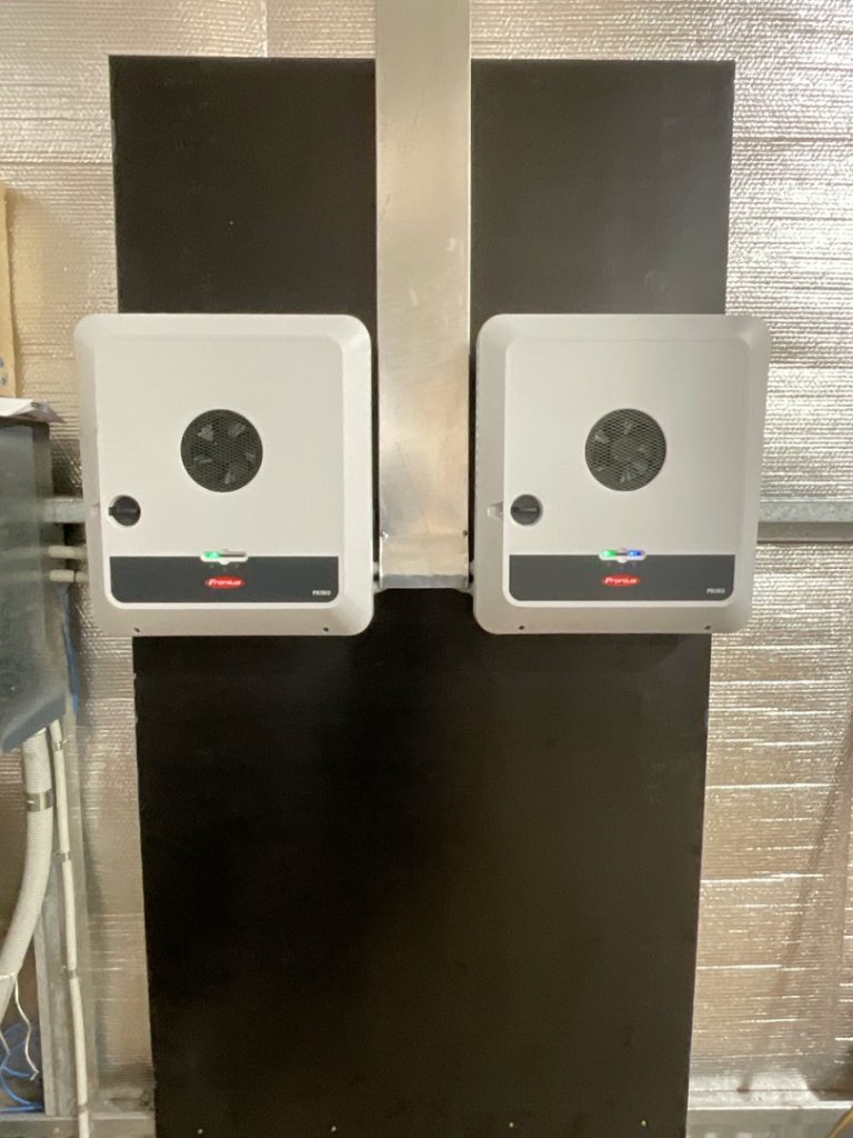 Two wall-mounted electric boxes with digital screens and status lights are installed side by side on a black panel in an industrial setting.