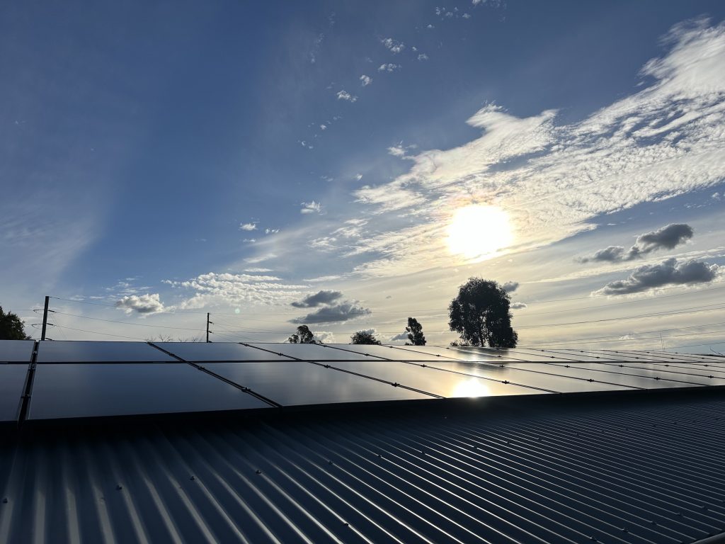 Solar panels installed on a rooftop under a partly cloudy sky with the sun shining brightly.