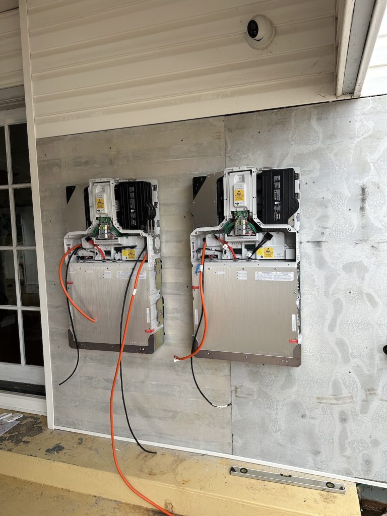 Two wall-mounted electrical control units with exposed wiring and equipment are installed on the exterior of a building.