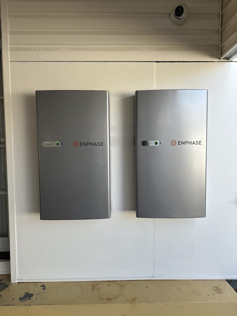 Two gray Enphase energy storage systems are mounted on a white wall. Both units have small indicator lights.