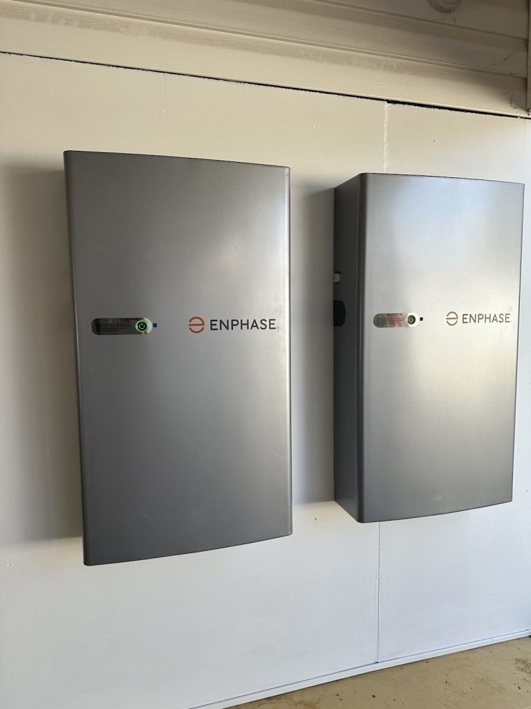 Two gray Enphase electrical storage units mounted on a white wall in a well-lit room.